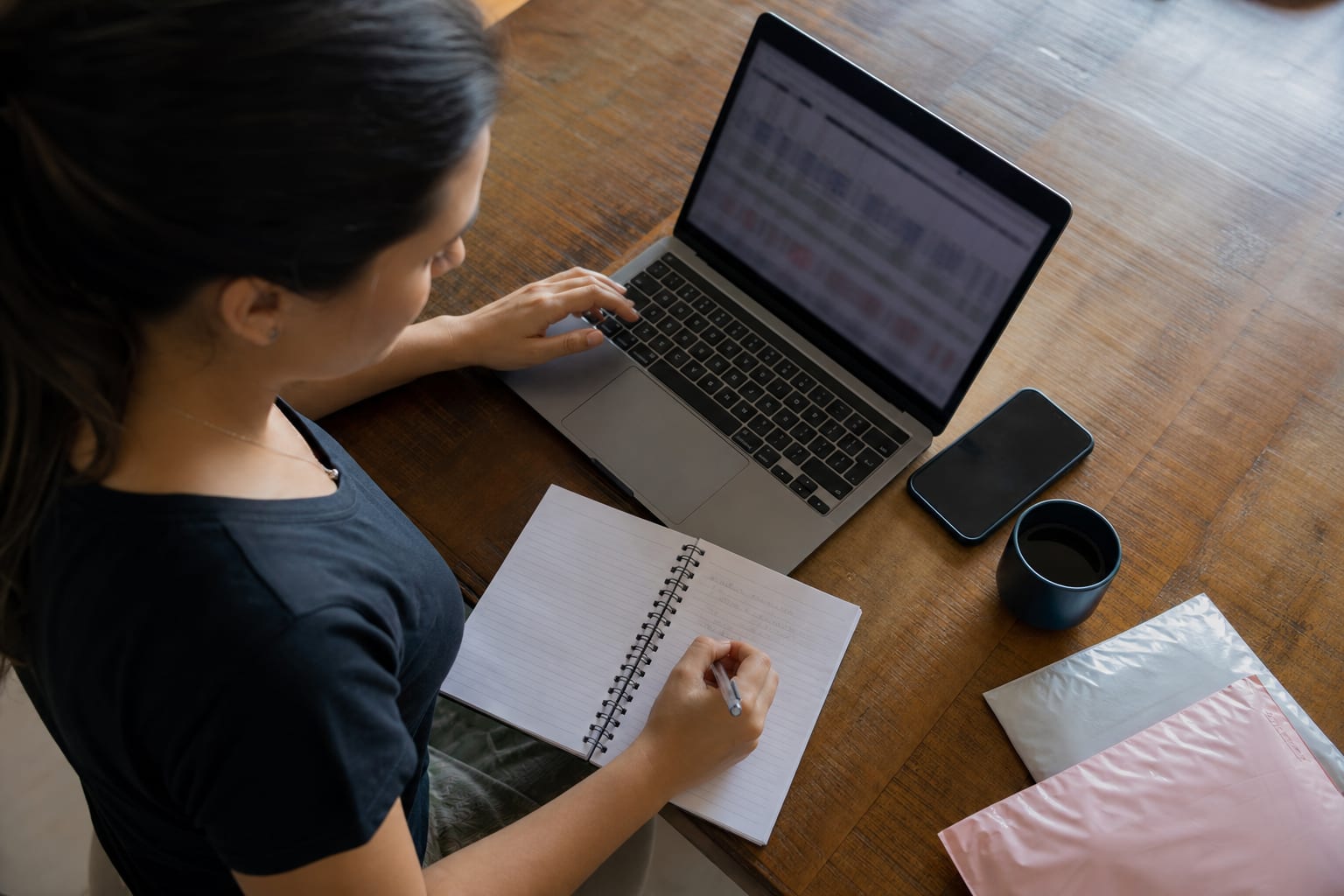 Mesa de trabalho vista de cima com notebook, caderno de anotações e envelopes de envio